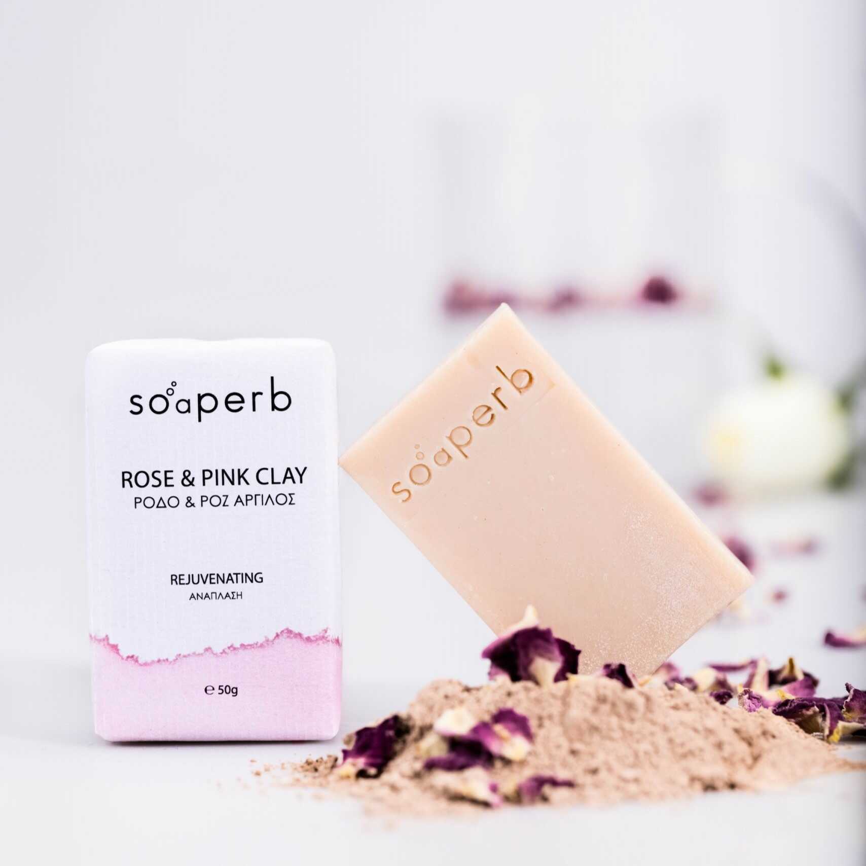 Natural soap bar "Rose & Pink Clay" by Soaperb – rejuvenating formula for mature skin with rosehip and pink clay. Product photo includes the soap and its packaging, surrounded by rose petals and pink clay powder. 50 g.